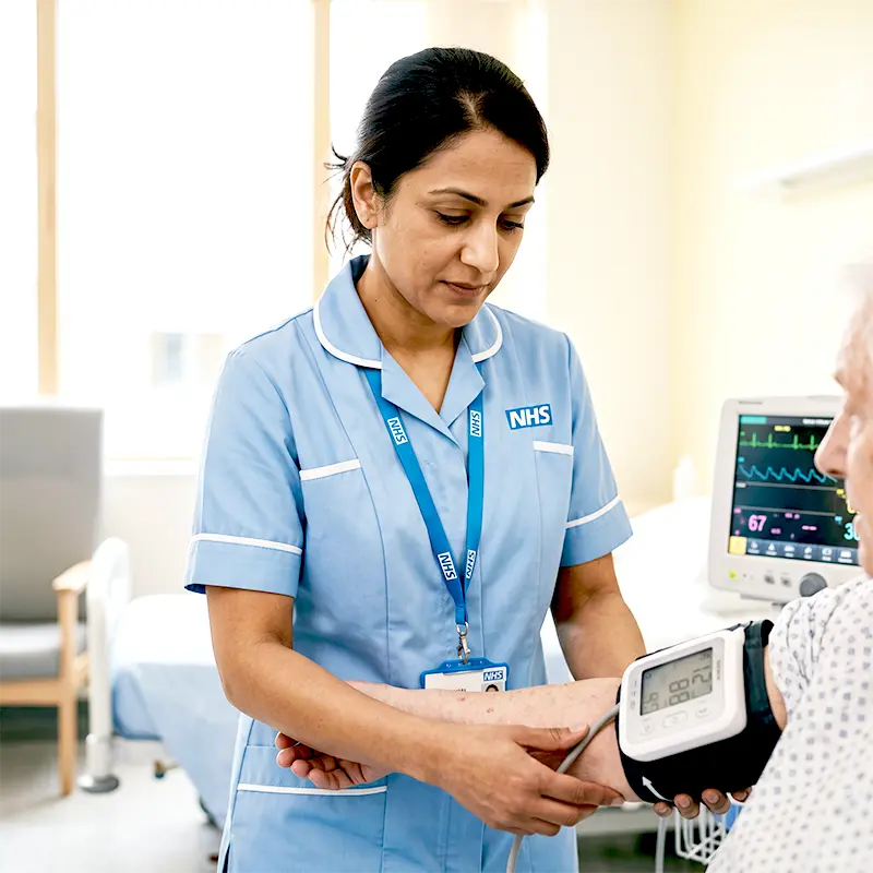 Healthcare support worker accurately taking patient vital sign observations on an NHS hospital bed.